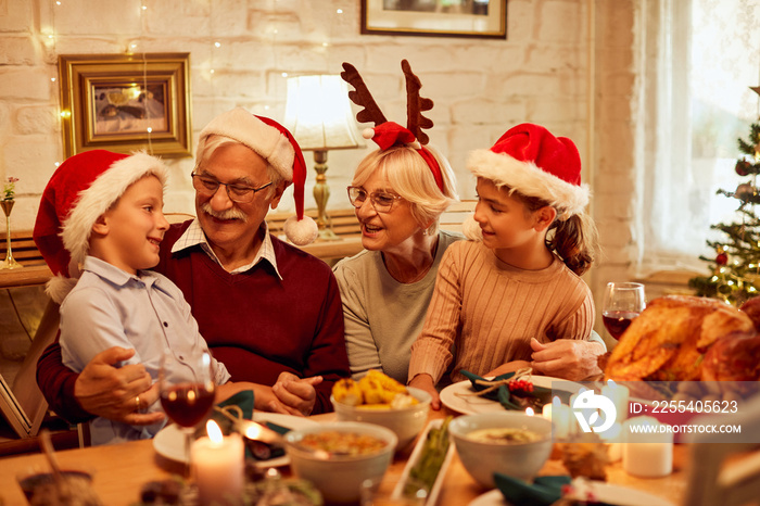 Happy kids talk to their grandparents during Christmas lunch at dining table.