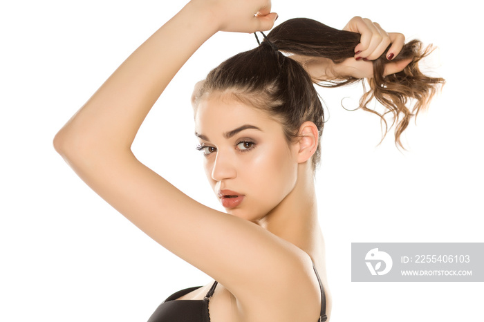 Young woman with makeup  tying her hair on white background