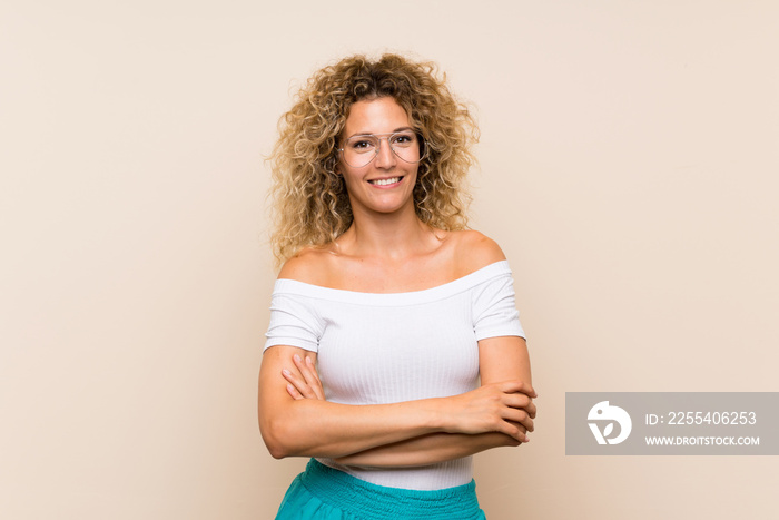 Young blonde woman with curly hair over isolated background with glasses and happy