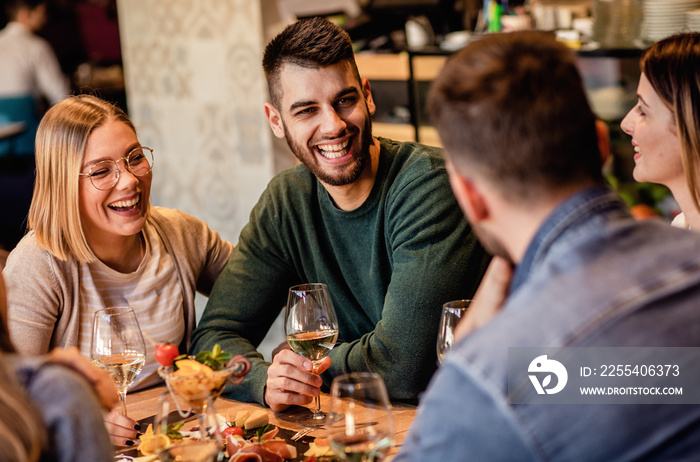 Group of young friends having fun in restaurant, talking and laughing while dining at table.