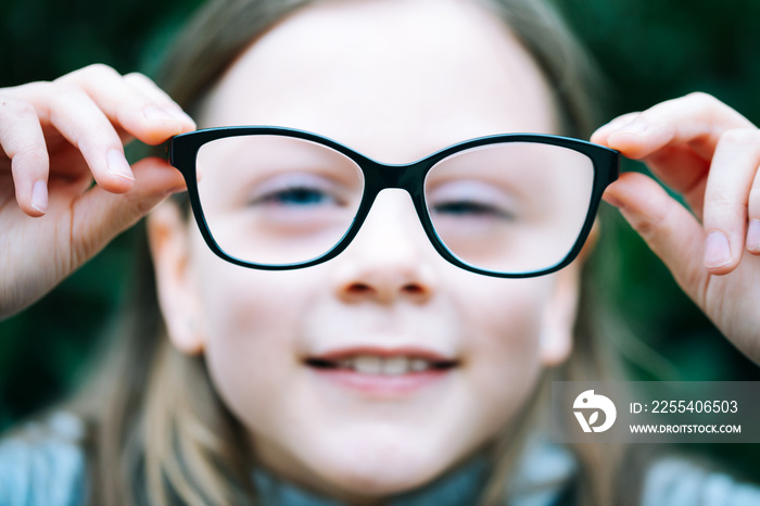 Closeup portrait of little girl  with myopia correction glasses. Girl is holding her eyeglasses right in front of camera with two hands - focus on glasses - shallow depth of field