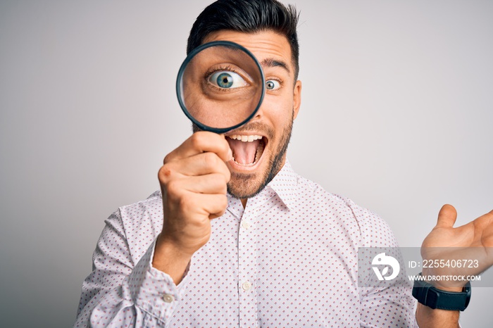 Young detective man looking through magnifying glass over isolated background very happy and excited, winner expression celebrating victory screaming with big smile and raised hands