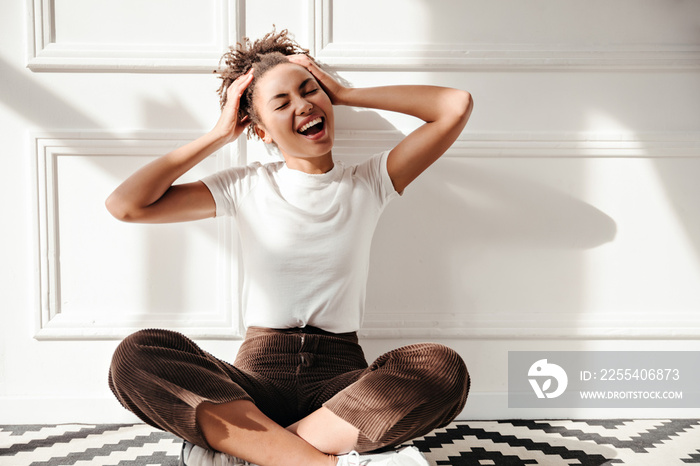 Carefree african american woman touching head. Laughing stylish black girl sitting on floor.