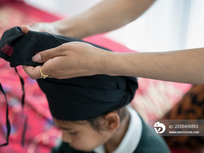 Mother wrapping traditional turban on son’s (6-7) head