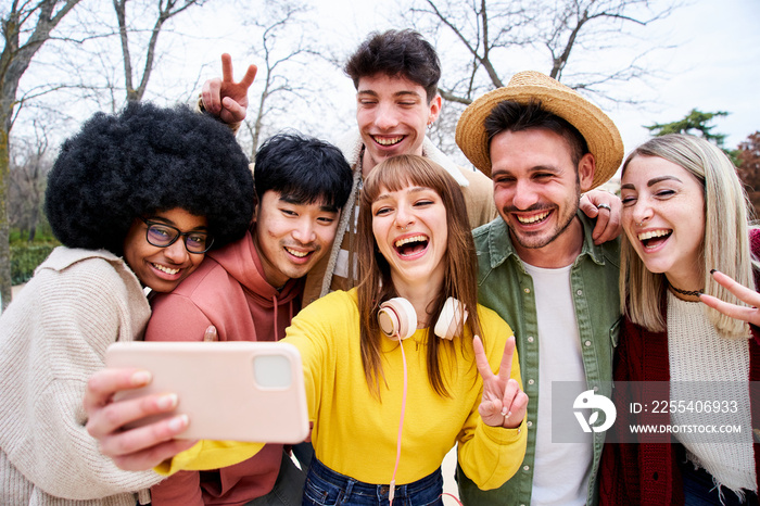 Group of smiling international teenage friends taking a selfie with Mobile cell in an urban park in autumn. Erasmus classmates using phone to upload content to social networks.