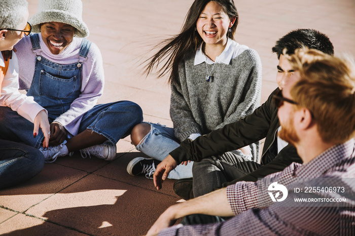 Multicultural group of friends laughing together sitting outside - Happy students having fun at college campus - Young people socializing smiling in the city - Happy friendship concept