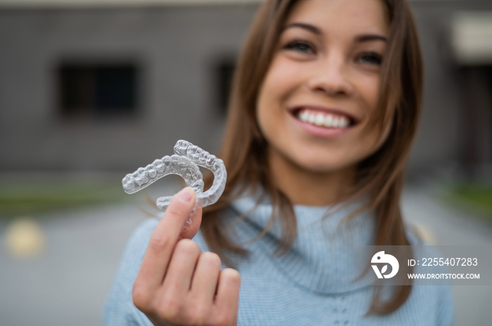 Caucasian woman with white smile holding transparent removable retainer. Bite correction device.