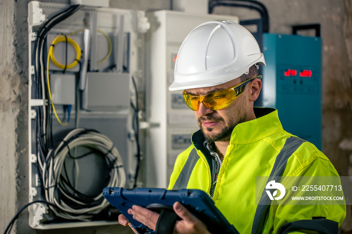 Man an electrical technician working in a switchboard with fuses, uses a tablet.