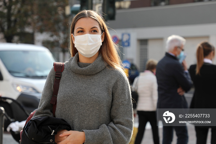 Portrait of young student woman walking in city street wearing surgical mask. Girl with face mask walks on road with people and traffic cars on the background.