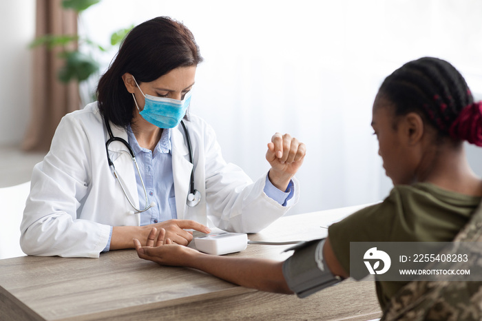 Military Healthcare. Doctor Wearing Medical Mask Measuring Blood Pressure For Soldier Woman