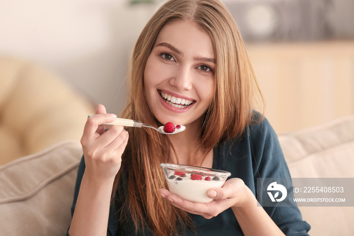 Young woman eating yogurt on sofa at home