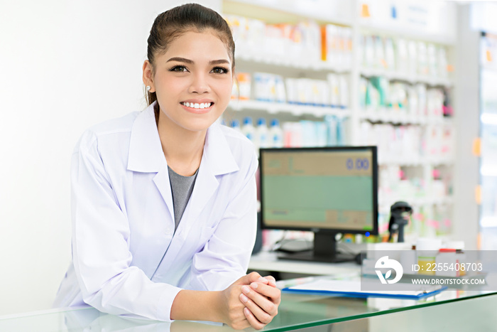 Smiling beautiful young Asian woman pharmacist in white gown coat at the counter in pharmacy