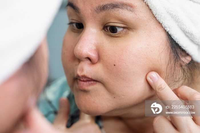 Plus size female examining her skin in the mirror