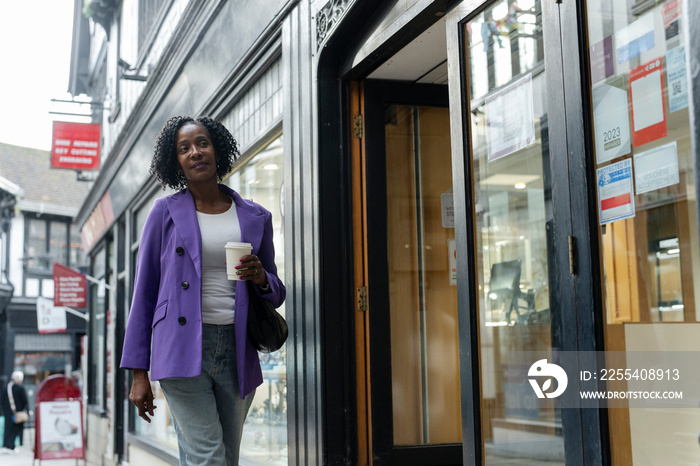 Confident woman walking with disposable cup in city