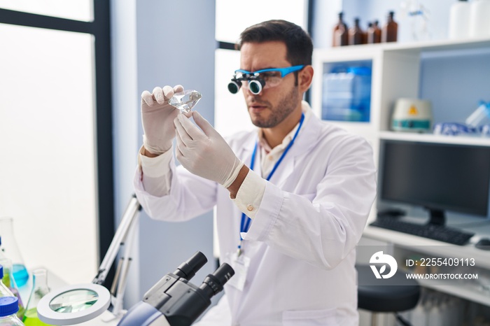 Young hispanic man scientist looking diamond by magnifying glasses at laboratory