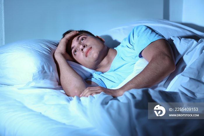 Young man suffering from insomnia while lying in bed at night