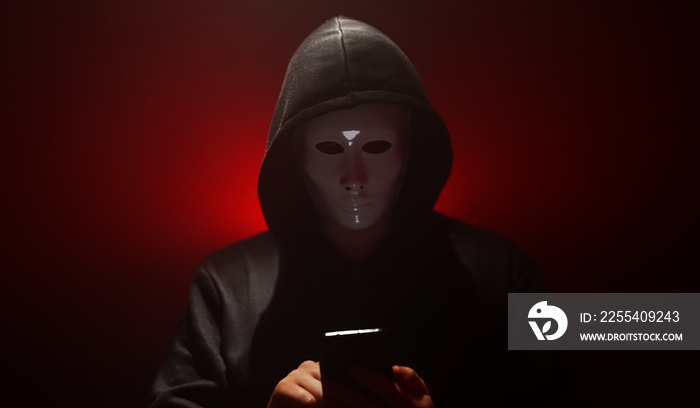 Man wearing mask with hoodie launches virus from smartphone.