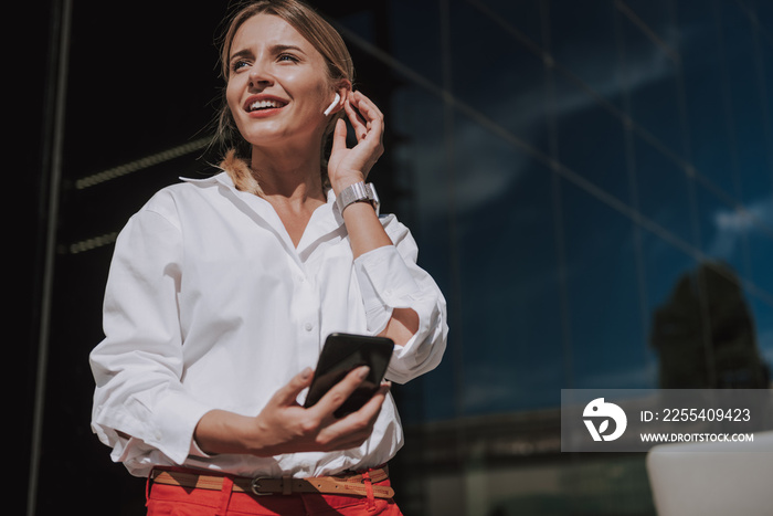 Waist up of pretty businesswoman with earpods looking away