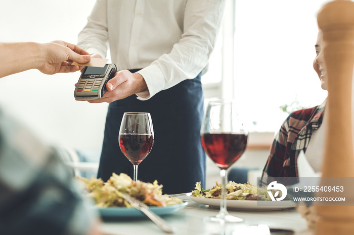 Payment with card. Nice professional waiter holding a money terminal while taking a payment