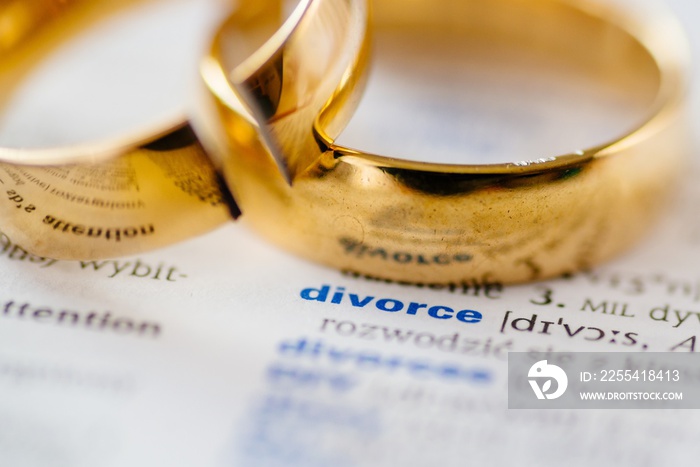 Two broken wedding rings on divorce word in dictionary.