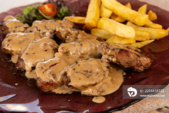 Plato de solomillo de cerdo con salsa de queso y patatas fritas.