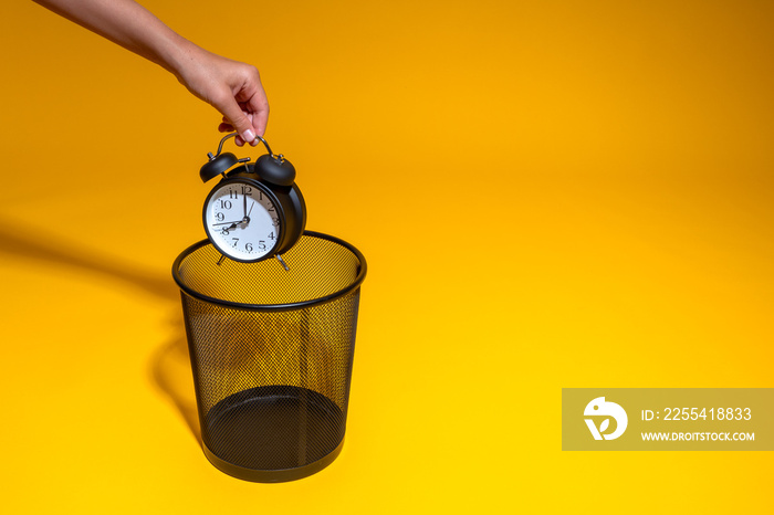 A hand holds an alarm clock over a trash can. The man throws away his watch and overslept for work again.