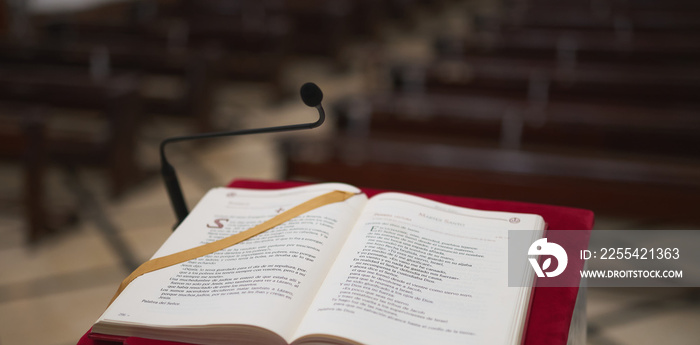 marble lectern with a red felt and a bible with some pews in the