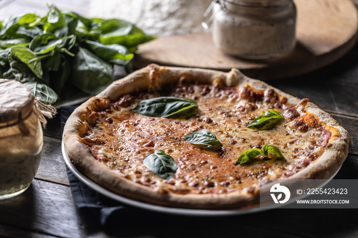 Pizza Napoli with tomato sauce, mozzarella and fresh basil, in the background flour and a jar of rye sourdough.