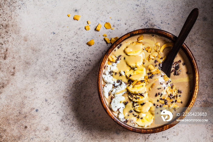 Chocolate smoothie bowl with coconut chips, banana and cocoa nibs in wooden bowl, top view. Healthy vegetarian breakfast concept.