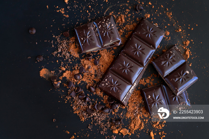 Broken chocolate bar pieces and cocoa powder on dark background