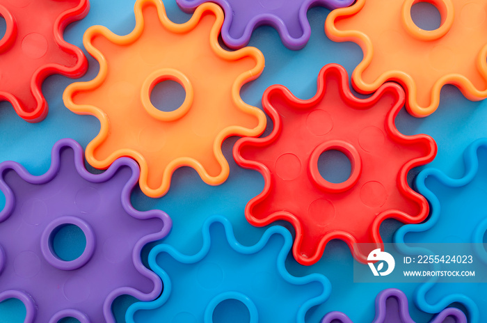 Teamwork and solidarity concept with photograph of connected colorful plastic toy gears with each gear a different color isolated on blue background