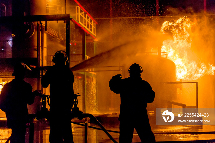 Firemen using water from hose for fire fighting at firefight training of insurance group. Firefighter wearing a fire suit for safety under the danger case.