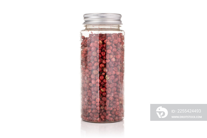 Lot of whole peruvian pink pepper in a plastic bottle isolated on white background