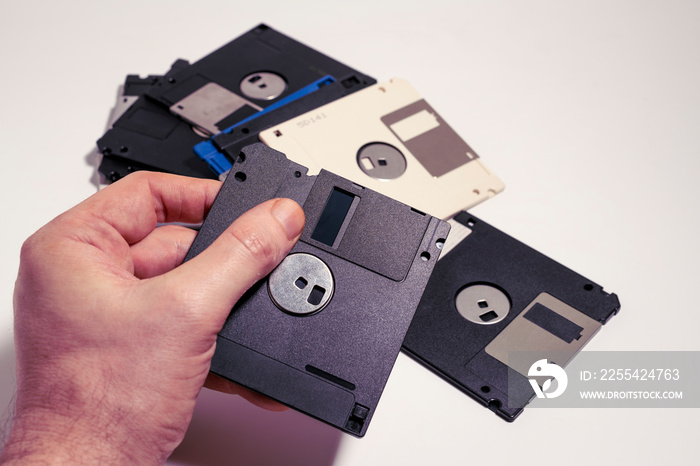 Man showing inside of a floppy disk on scattered floppy disks. Old computer technology from 1980s and 1990s.