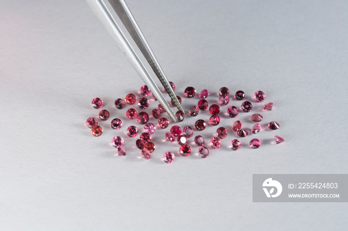 Scattering of natural rich cherry, raspberry rich red round genuine spinel gemstones. Colorful matched small natural unheated spinel gemstone faceted settings. One stone in tweezers. White background.