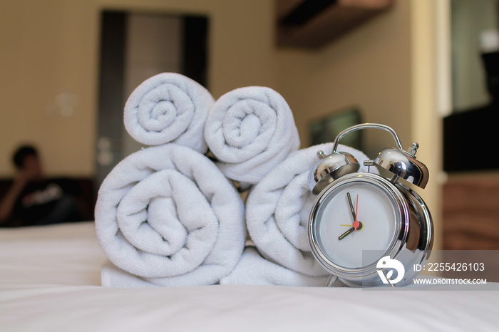 alarm clock sits next to clean white spa towels that are folded up for guests staying in resort and placed on top of their mattresses as towels are must when they need to take shower before resting.