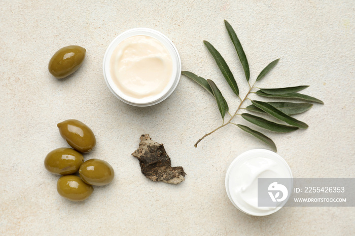 Jars of cream with green olives, plant branch and tree bark on white background