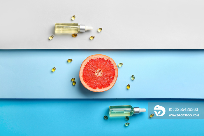 Cosmetic dropper bottles with pills and grapefruit on color background