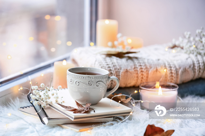 Beautiful autumn composition with burning candles and cup of tea on window sill