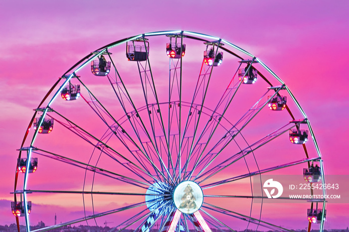 Closeup colorful ferris wheel against sunset pink sky.