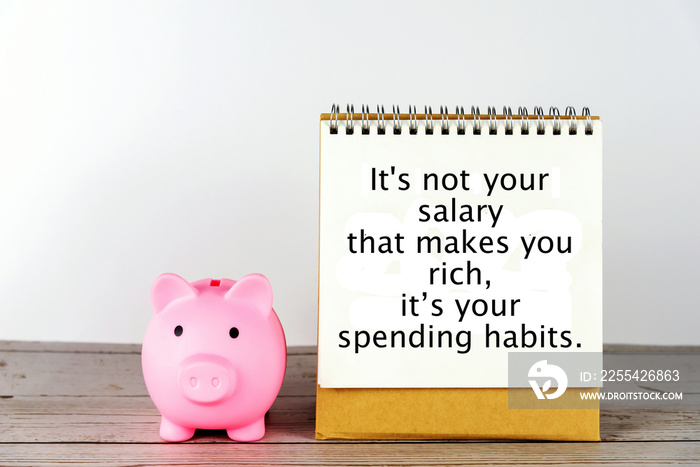 Piggy bank and Positive finance planning motivational quote on spiral sitting calendar page on the table. It’s not your salary that makes you rich, but your spending habits.