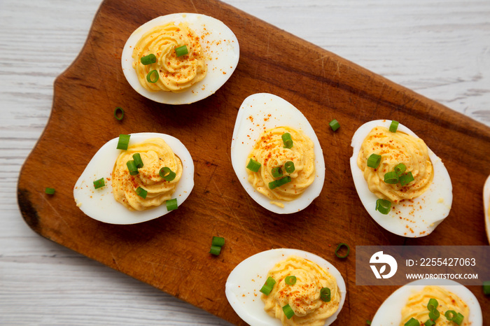 Homemade Deviled Eggs with Chives on a rustic wooden board on a white wooden background, top view. Flat lay, overhead, from above.