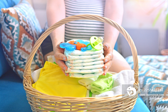 Pregnant woman packing bag for maternity hospital at home. Preparing for newborn birth. Future mom holding stack of diapers above the basket.