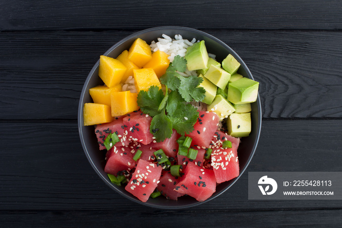 Poke salad in the dark bowl in the center of the black wooden background.Top view.Closeup.