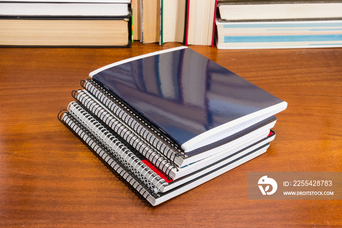 Stack of different exercise books on table against of books