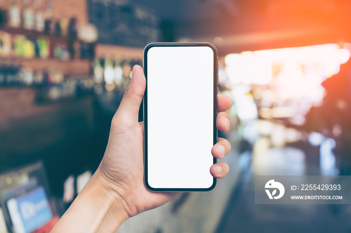 Man’s hand shows mobile smartphone with white screen in vertical position, Blurred or Defocus image of Coffee Shop or Cafeteria for use as Background vintage tone. - mockup template and clipping path