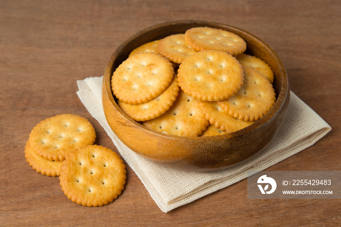 Round salted cracker cookies in wooden bowl putting on linen and wooden background.