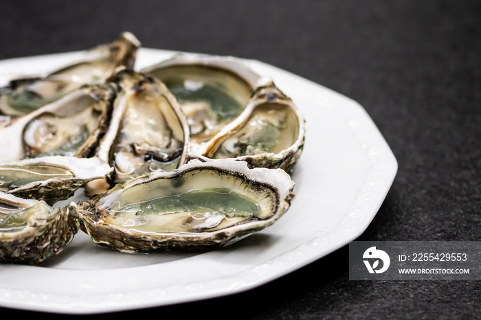 Fresh oysters ready to be eaten raw. Oysters on a plate and a black stone. Raw fish oysters, luxurious dinner and quality fresh shellfish.  Restaurant special dish