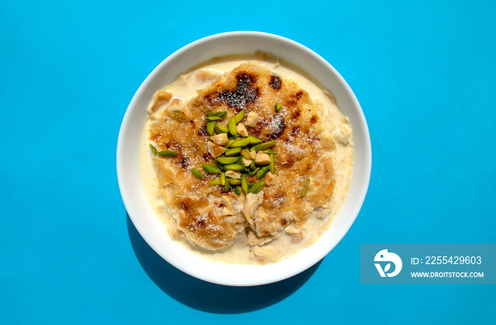 Traditional Arabic, oriental dessert Om Ali. Top view. Egyptian Bread Pudding in a white bowl on blue background. Top view. Egypt sweet pastry dessert