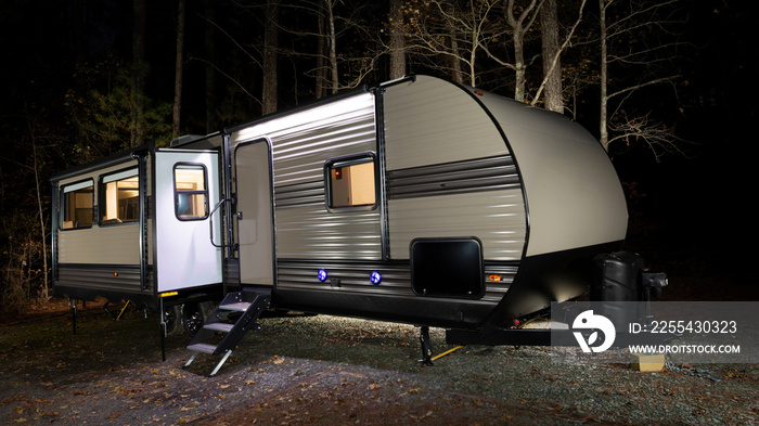 Camper trailer at a late fall campsite with lights on inside and dark forest behind the RV